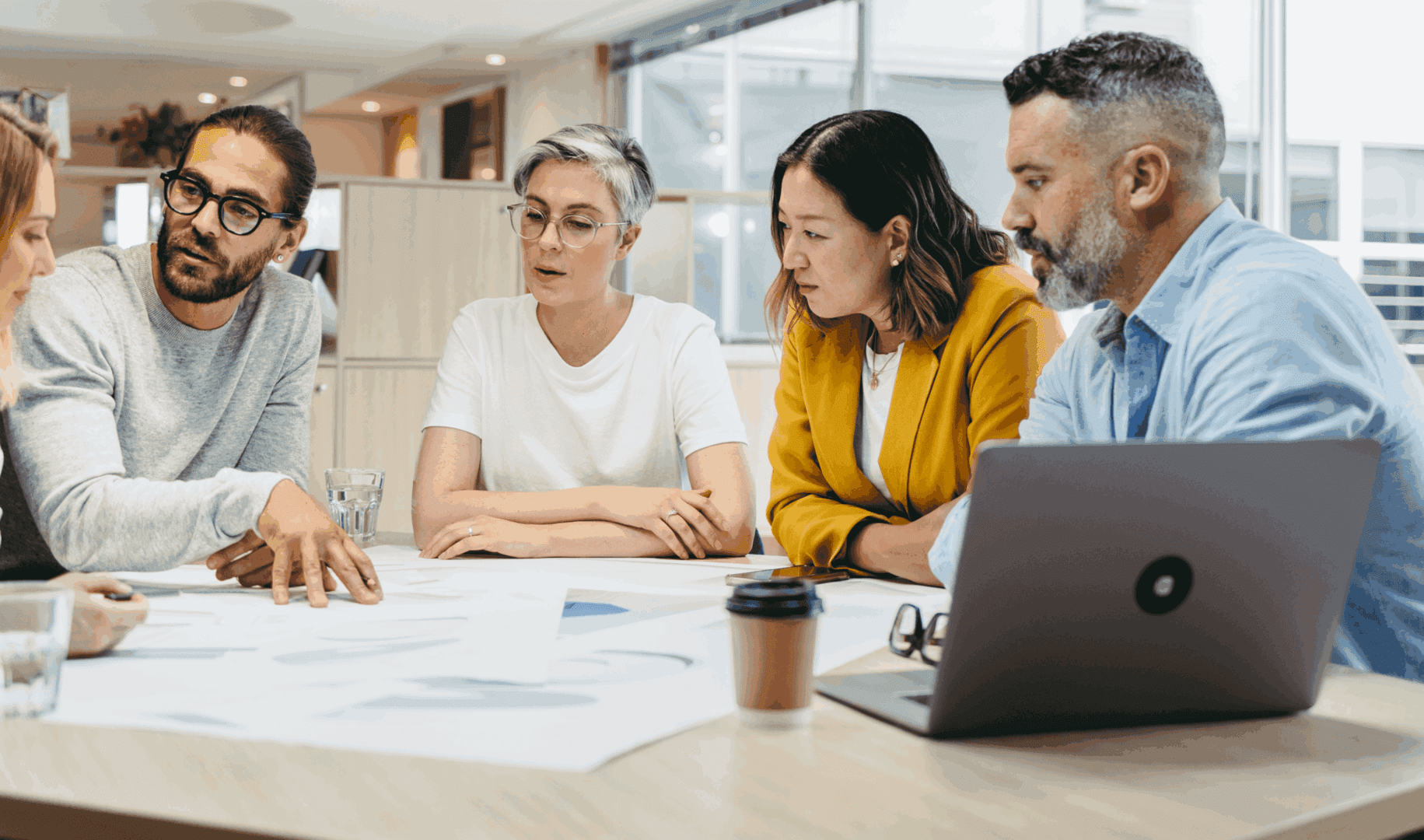A group discussing work plans around a table with documents and a laptop.
